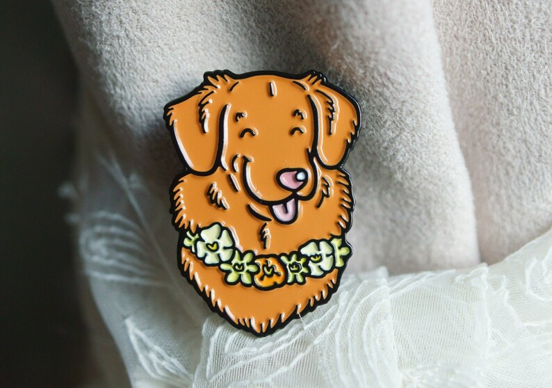 A Toller enamel pin badge shown propped on cream-coloured fabric and white lace.