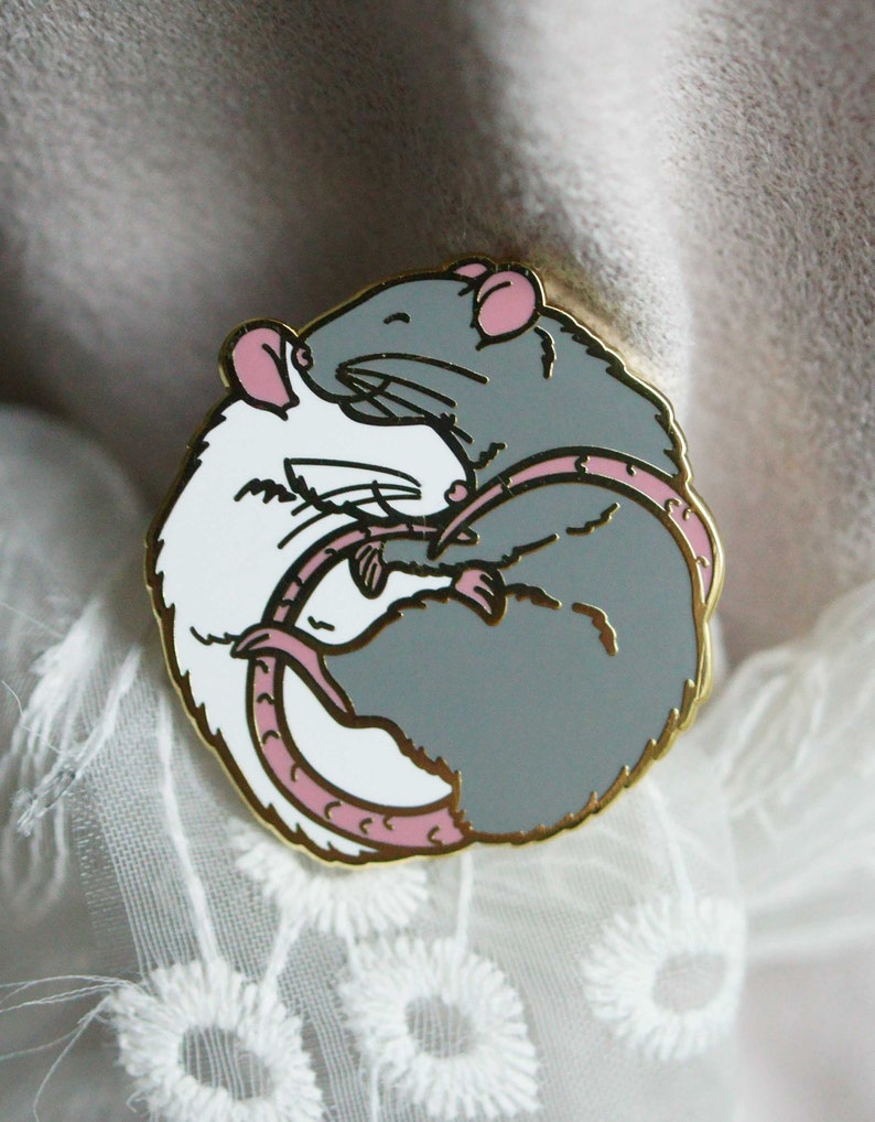 An enamel pin showing two hugging rats, a white rat on the left and a grey/blue rat on the right. The plating colour is gold.