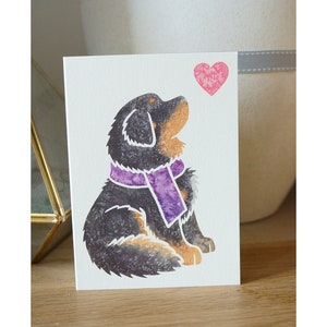 May include: A greeting card featuring a black and brown dog with a purple scarf looking up at a pink heart.