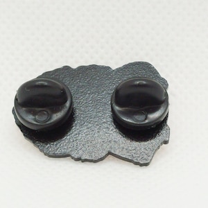 The reverse of a Toller pin badge. The metal colour is black and textured. There are two black rubber clutches attached, one at either end (top and bottom of the pin when displayed correctly).