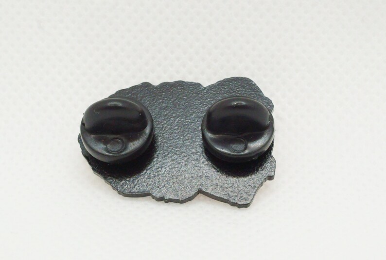 The reverse of a Toller pin badge. The metal colour is black and textured. There are two black rubber clutches attached, one at either end (top and bottom of the pin when displayed correctly).