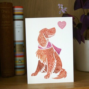 May include: A watercolor illustration of a dog wearing a pink scarf, looking up at a pink heart. The illustration is on a white card.