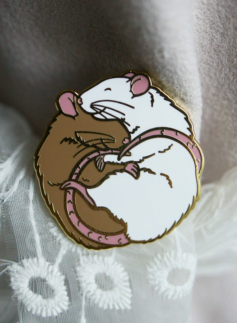 A circular enamel pin showing two sleeping rats embracing. The left hand rat is brown/agouti and the right hand one is white. The plating (outline) colour is gold.