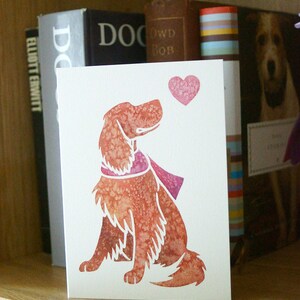May include: A white card with a red heart and a watercolor illustration of a brown dog with a pink scarf. The dog is looking up at the heart.