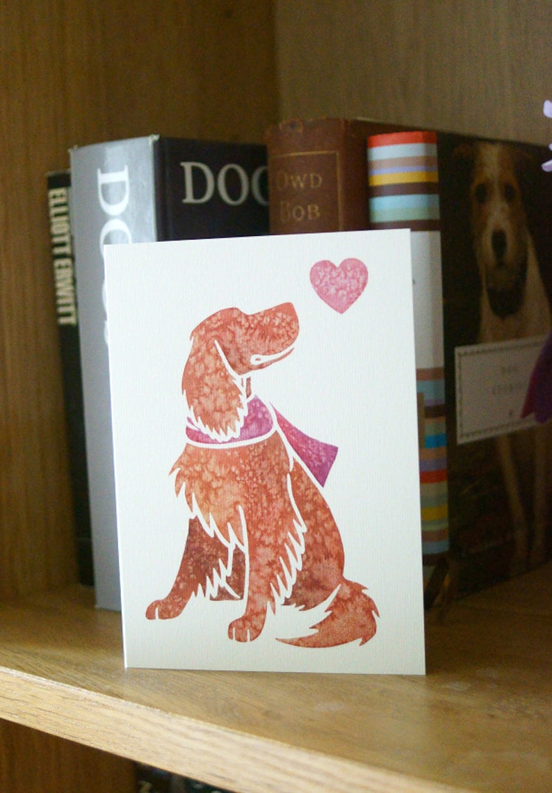 May include: A white card with a red heart and a watercolor illustration of a brown dog with a pink scarf. The dog is looking up at the heart.