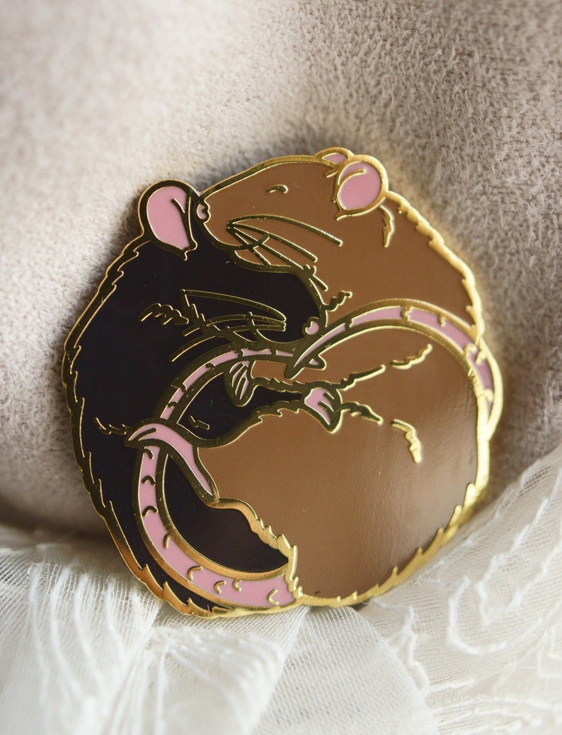 An enamel pin featuring two sleeping rats cuddled up in a circle. The left hand side rat is black and the right hand side is brown/agouti.