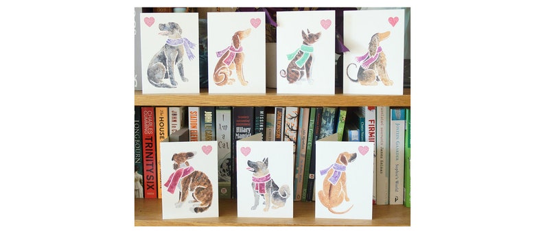 May include: Set of eight greeting cards featuring watercolor illustrations of dogs wearing scarves. Each card has a pink heart in the top right corner.