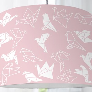 Op de afbeelding: Een roze lampenkap met een wit origami-vogelpatroon.