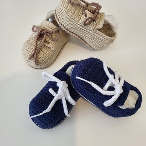 May include: Two pairs of crocheted baby shoes. One pair is beige with brown laces and the other pair is navy blue with white laces.
