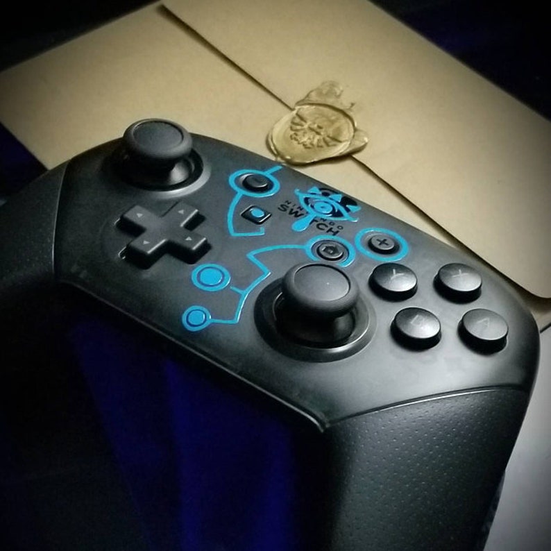 May include: A black Nintendo Switch controller with a blue and white design featuring the Triforce symbol and the words "Nintendo Switch".