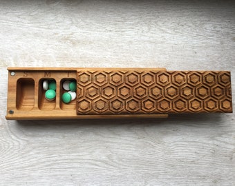 May include: Wooden pill box with a hexagonal pattern lid. The box has seven compartments labeled "S", "M", "T", "W", "Th", "F", and "Sa". The box is filled with green and white pills.