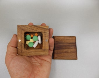 May include: A wooden box with a hinged lid, open to reveal a compartment filled with colorful pills. The box is made of dark wood with a natural grain pattern.