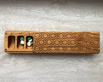 May include: Wooden pill box with a honeycomb pattern on the lid. The box has seven compartments labeled S, M, T, W, T, F, S. There are pills in the compartments labeled S, M, and T.