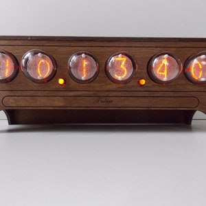 May include: A wooden clock with six Nixie tubes displaying the time 01:34:00. The clock has a brown wooden case with a label that reads "Pulsar".