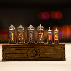 May include: A wooden clock with six clear glass tubes displaying the numbers 101715. The clock has a brown wooden base with a logo on the front.