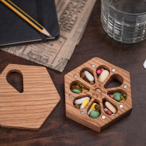 May include: A wooden hexagonal pill box with seven compartments, each containing different colored pills. The box is made of light brown wood and has a natural wood finish. The box is sitting on a dark brown wooden surface.