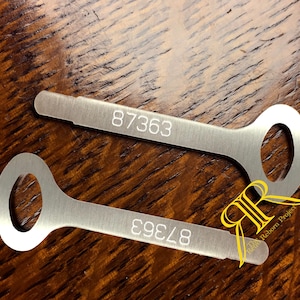 以下が含まれることがあります： 丸いヘッドと長方形のシャフトを持つ、銀色の平らな金属製の鍵が2本。各鍵のシャフトには数字の87363が刻印されています。画像の右下には、The Reborn Projectというテキストが入った黄色のロゴが表示されています。