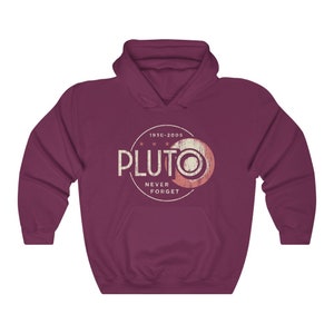 May include: A maroon hooded sweatshirt with a vintage-style graphic of Pluto, a planet that was reclassified as a dwarf planet in 2006. The graphic includes the text "Pluto" in a white circle with the text "1930-2005" above it and "Never Forget" below it.
