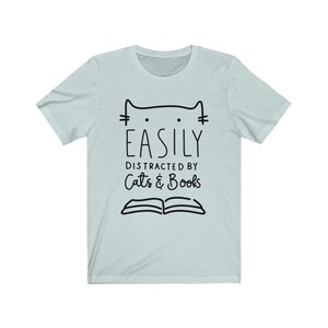 May include: Light blue t-shirt with a black cat illustration and the text "Easily Distracted by Cats & Books".