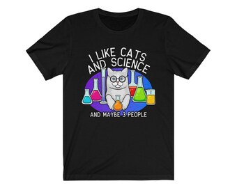 May include: Black t-shirt with a white cat wearing glasses and surrounded by colorful beakers. The text on the shirt reads "I like cats and science and maybe 3 people."