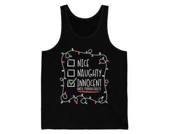 May include: Black tank top with the text "NICE, NAUGHTY, INNOCENT" in white, with a green checkmark next to "INNOCENT". The text is framed by a string of colorful Christmas lights. The phrase "UNTIL PROVEN GUILTY" is below the text.