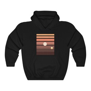 May include: Black hooded sweatshirt with a graphic print of a sunset with two planets. The graphic is a minimalist design with a series of horizontal stripes in shades of orange, brown, and red.