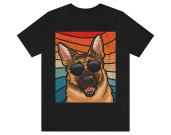 May include: A black t-shirt with a retro-style illustration of a German Shepherd dog wearing sunglasses. The dog is set against a colorful striped background.