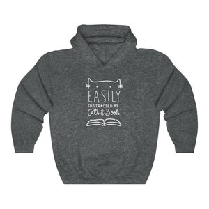 May include: A dark gray hooded sweatshirt with a white outline of a cat and the text "EASILY DISTRACTED BY Cats & Books".