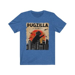 May include: A blue t-shirt with a vintage-style graphic of a pug standing on a city skyline. The graphic says "Pugzilla -  パグジラ - "