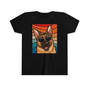 May include: A black t-shirt with a retro-style image of a German Shepherd wearing sunglasses. The dog is looking to the right and has a happy expression. The background is a colorful sunset.
