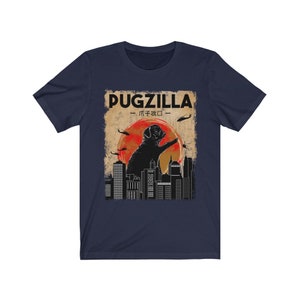 May include: A navy blue t-shirt with a vintage-style graphic of a pug standing on a city skyline. The graphic says "Pugzilla -  パグジラ - ".