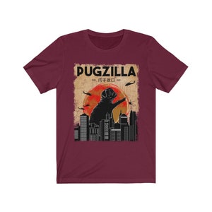 May include: A maroon t-shirt with a graphic of a pug standing on a city skyline. The text "PUGZILLA -  パグジラ - " is above the pug.