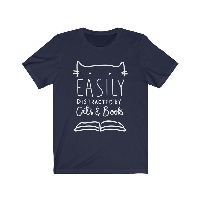 May include: Navy blue t-shirt with a white outline of a cat and an open book. The text "Easily Distracted by Cats & Books" is printed on the shirt.