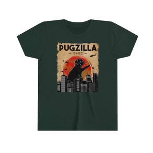 May include: A green t-shirt with a graphic of a pug standing on a city skyline. The graphic is in a retro style with a red sun and helicopters flying overhead. The text "PUGZILLA - パグジラ -" is printed on the graphic.