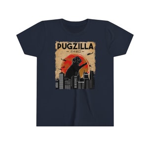 May include: A navy blue t-shirt with a vintage-style graphic of a pug standing on a city skyline. The graphic says "Pugzilla -  パグジラ - ".