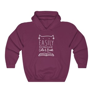 May include: A maroon hooded sweatshirt with a white graphic design that says "Easily Distracted by Cats & Books" with a cat head and an open book.