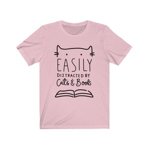 May include: Pink t-shirt with a black cat illustration and the text "Easily Distracted by Cats & Books".