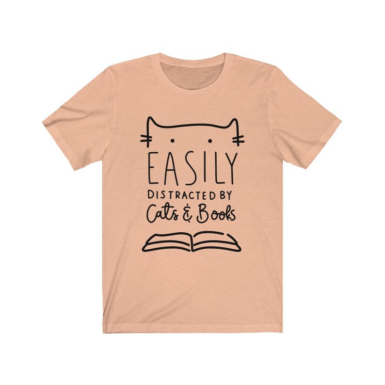 May include: A peach-colored t-shirt with a black cat illustration and the text "EASILY DISTRACTED BY Cats & Books".