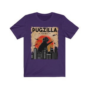 May include: Purple t-shirt with a vintage-style graphic of a pug standing on a city skyline. The graphic says "Pugzilla -  パグジラ - "