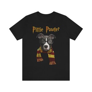 May include: Black t-shirt with a gray pit bull wearing glasses and a red and yellow scarf. The text "Pittie Pawter" is printed in gold above the dog.