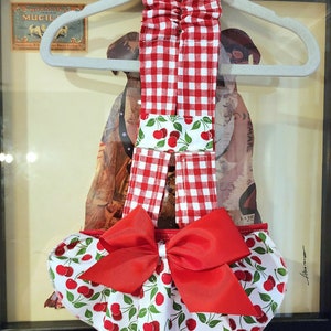 May include: Red and white gingham baby romper with a cherry print and a large red bow.