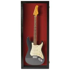 May include: Black electric guitar displayed in a black wood frame with a red velvet backing.