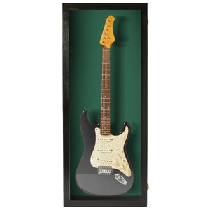 May include: A black electric guitar with a white pickguard and gold hardware is displayed in a black wood frame with a green felt backing.