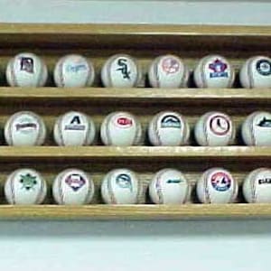 May include: A wooden display case with three shelves holds a collection of baseballs. Each baseball has a different team logo printed on it. The logos include the Chicago Cubs, New York Yankees, Boston Red Sox, and more.