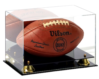 May include: A brown leather football with white laces and the text "Wilson", "Official", "Duke Pattern", and "Made in USA" is displayed in a clear acrylic display case with a black base and gold accents.