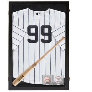 May include: A black framed display case containing a white baseball jersey with black stripes and the number 99 on the back. A wooden baseball bat and two baseballs are also displayed in the case.