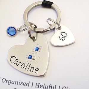 May include: Silver heart-shaped keychain with the name Caroline engraved on it, a blue rhinestone charm, and a smaller heart-shaped charm with the number 60 engraved on it.