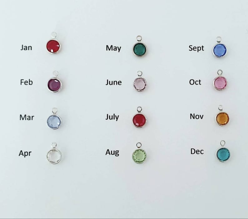 May include: Twelve small round charms with different colored crystals, each charm representing a month of the year. The charms are labeled with the month's abbreviation: Jan, Feb, Mar, Apr, May, June, July, Aug, Sept, Oct, Nov, Dec.