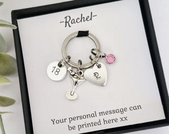 May include: Silver keychain with charms, including a heart, a martini glass, and a disc with the number 18. A pink gem and the name "Rachel" are also featured. The text "Your personal message can be printed here xx" is printed on the card.
