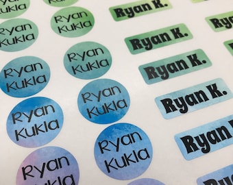 May include: A variety of colorful round and rectangular stickers with the name "Ryan Kukla" printed in black text. The stickers have a watercolor effect with different shades of blue, green, and purple.